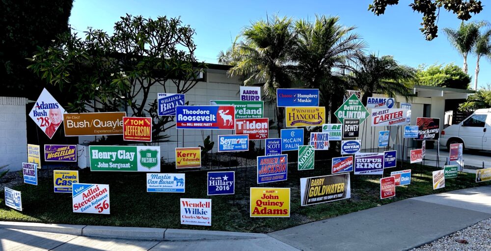 Front yard of home located on street corner with 58 colorful yard signs installed on the front lawn. Each sign bearing the name of former candidates for US President that lost their election.